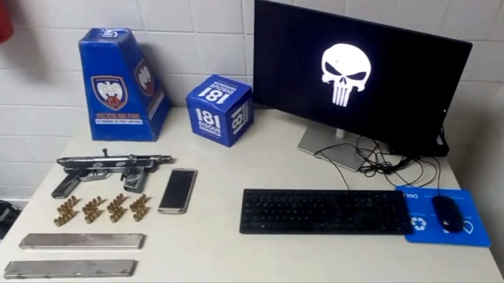 Polícia Militar apresentando apreensões de armas, após prisão de um sujeito sobre uma mesa uma metralhadora, semi industrial, 45 munições 9mm, dois pentes e um celular.