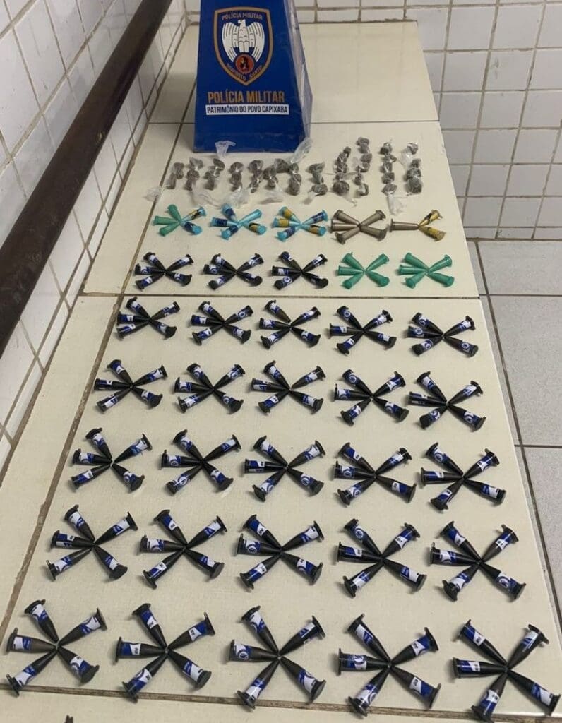 Sobre uma mesa branca 660 pinos de cocaína, 28 pedras de crack e 27 buchas de maconha, apreendidas pelas equipes da Policia Militar.