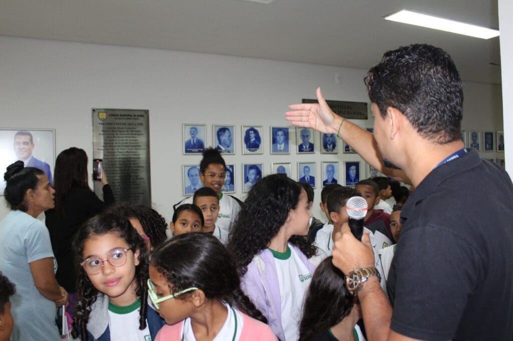 Leo Gomes com um microfone em mãos explicando os funcionamentos da Câmara da Serra em um corredor com varias crianças ao seu redor.