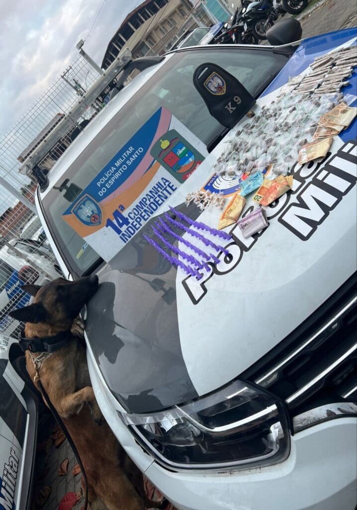 o cão da Polícia Militar Zorg ao lado de uma viatura e sobre o capo do veículo centenas de entorpecentes e dinheiro em espécie.