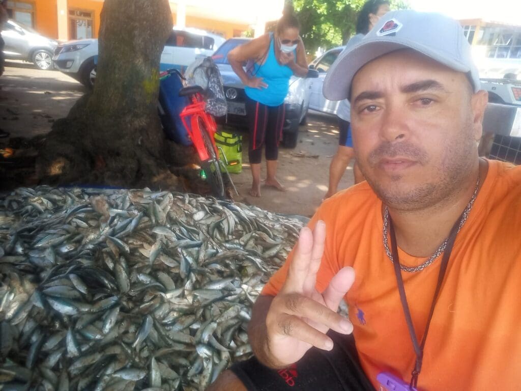 Janjao pousando para foto, ao lado de peixes que acabaram de ser retirados do mar na praia de Manguinhos.