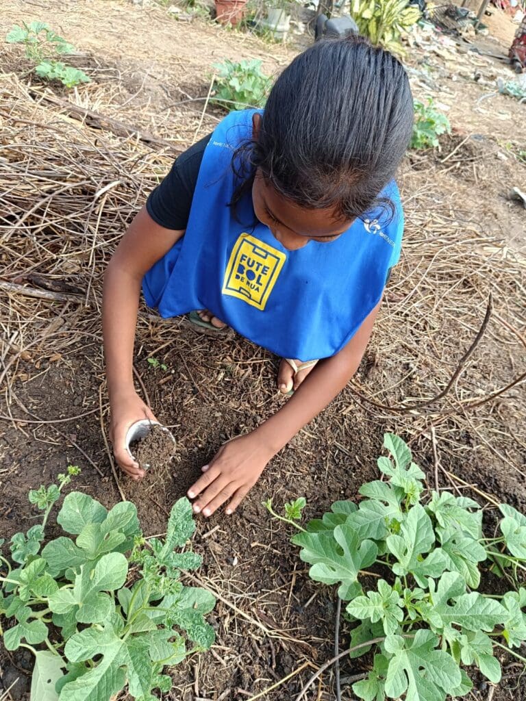 Projeto Futebol de Rua, uma menina aprendendo a plantar alguns legumes na Orta da instituição.