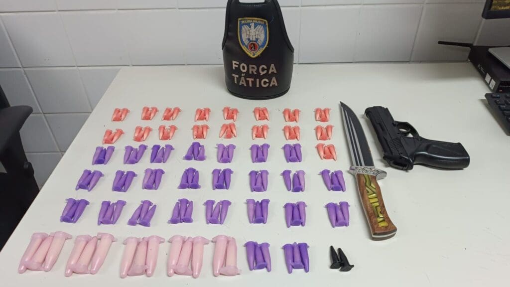 Materiais apreendidos pela equipe da Polícia Militar no bairro de Nova Almeida, sobre uma mesa 112 pinos de cocaína, um simulacro de arma de fogo e uma faca.
