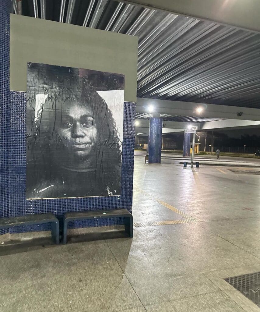 Uma foto preta e branca de uma jovem colada em uma parede de um terminal de ônibus da Serra.