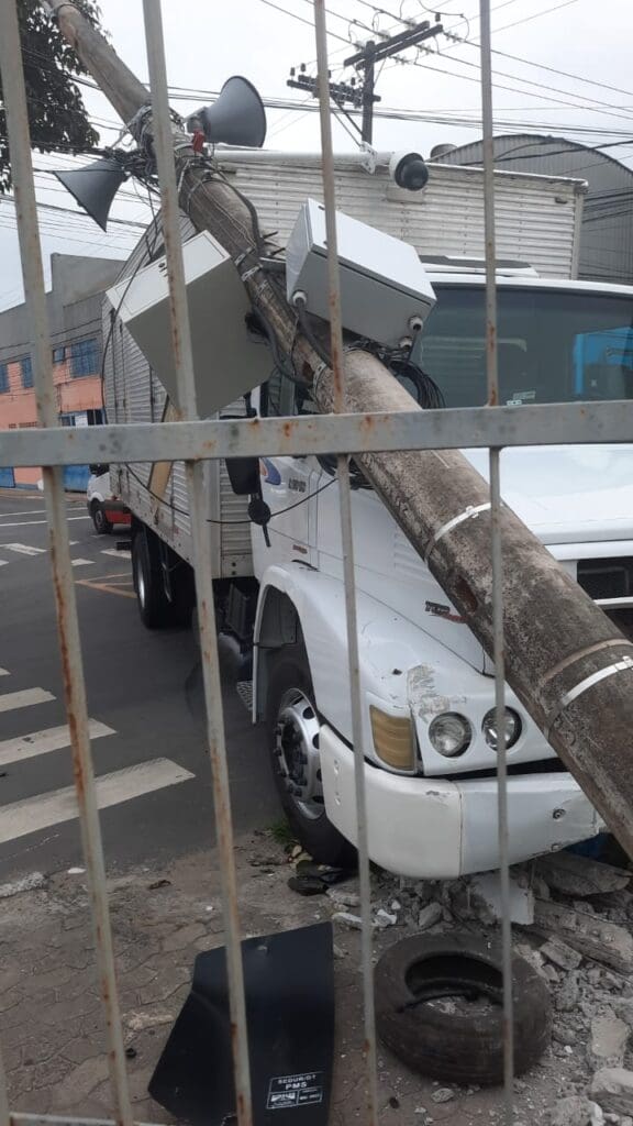 Imagem de um cruzamento, após um acidente, com um caminhão colidido em um poste.