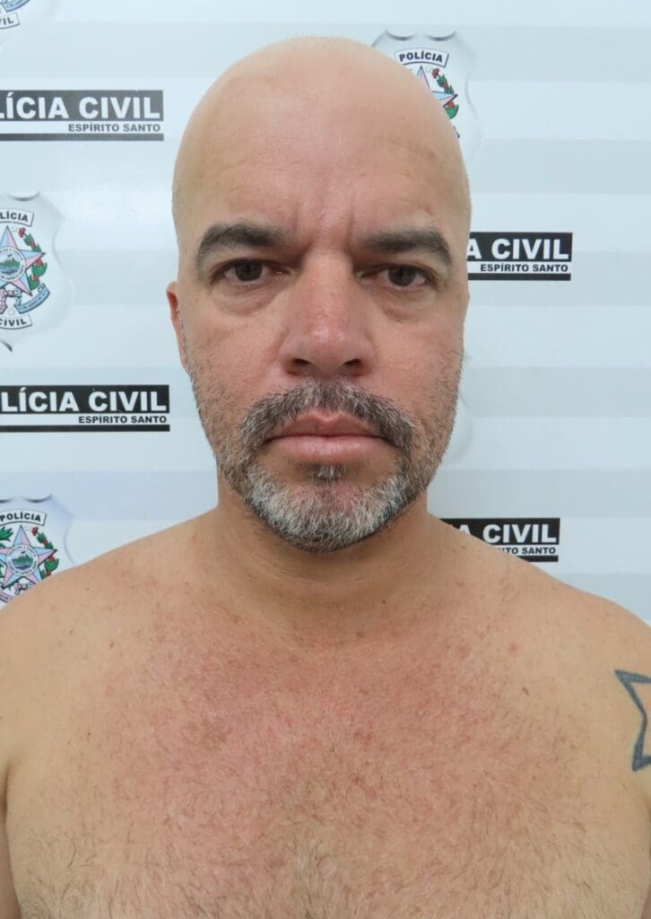 A fotografia de homem em frente a um banner da Polícia Civil, após ser preso (Diógenes de Freitas dos Santos).