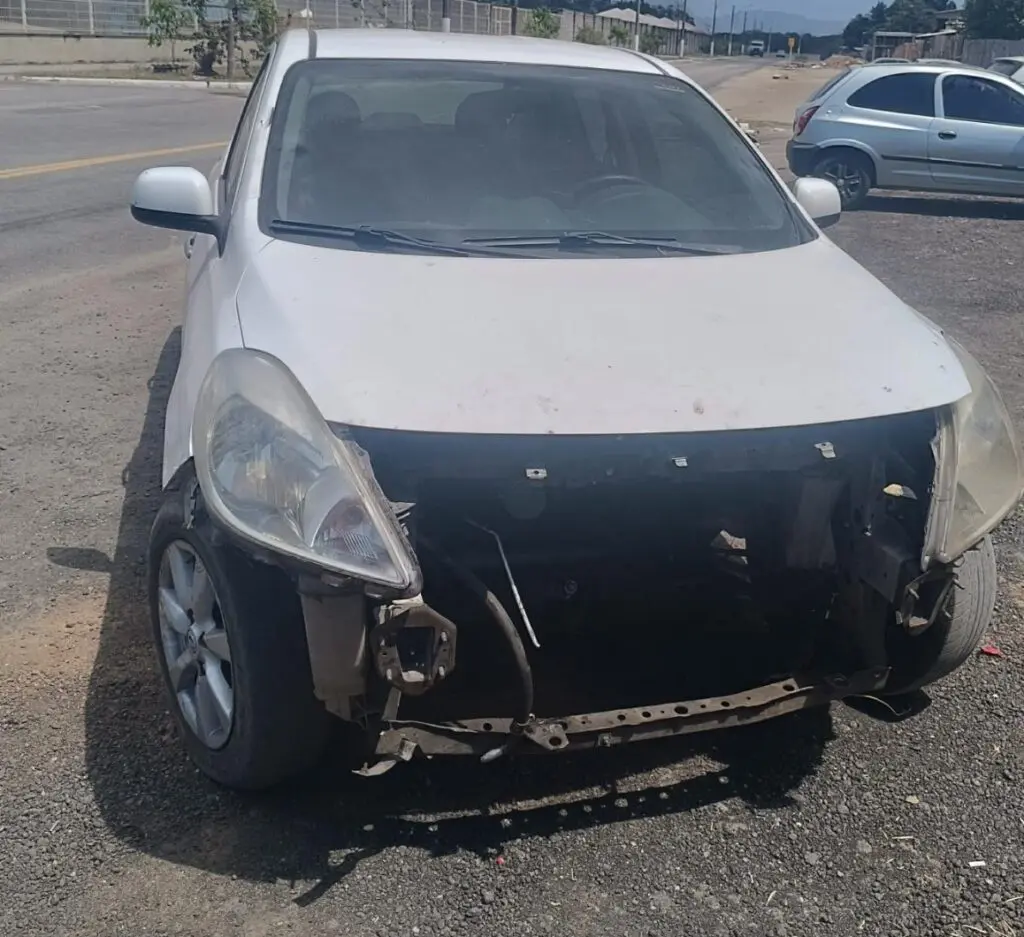 Um veículo, Nissan Versa branco, com a parte frontal danificada.