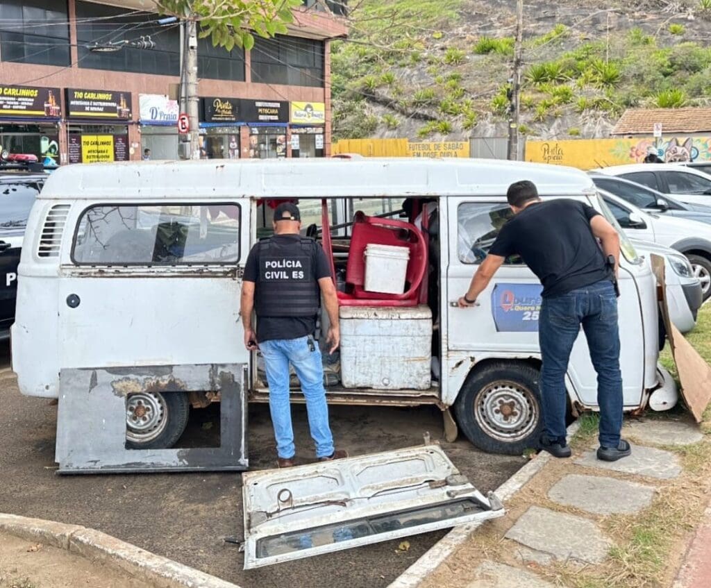 Dois policiais civis realizando buscas em um veículo modelo Kombi, onde um sujeito acusado de latrocínio morava.