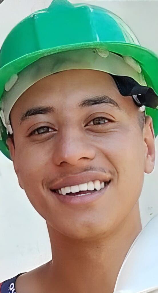 Imagem de um jovem sorridente usando um capacete de proteção de construção civil, (Ronald da Silva Modesto, de 19 anos).