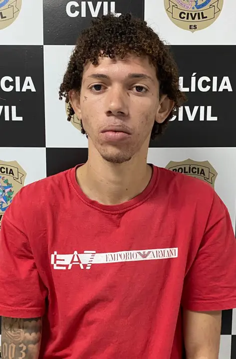 Imagem de um homem identificado como sendo Davi de Oliveira Santos, vulgo "Cabelinho", posando para a foto em frente ao banner da Polícia Civil, após ser preso.