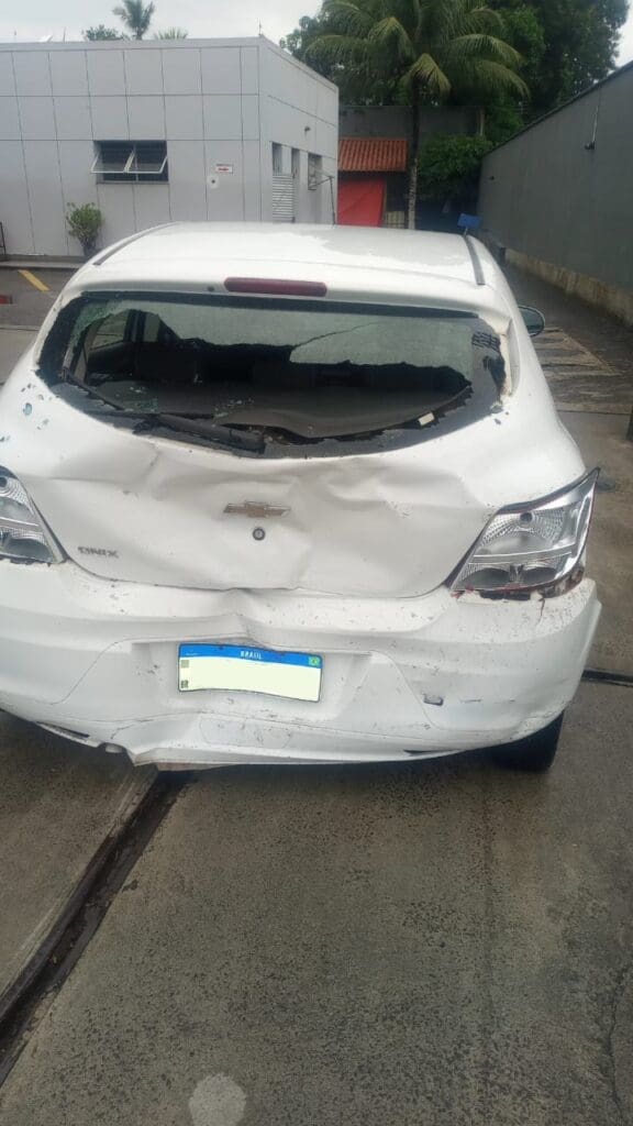 Veículo da vítima após o acidente, com a parte traseira totalmente amassada, estacionado em um posto de combustíveis. 