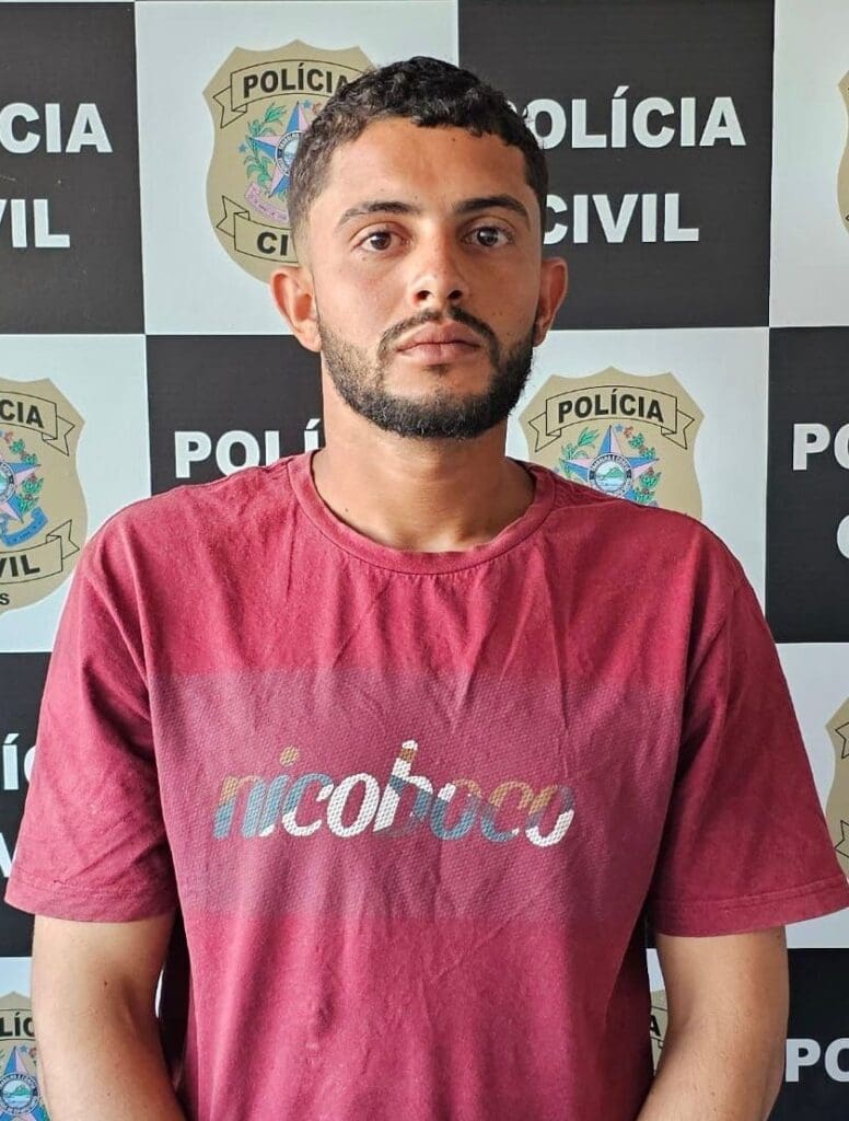 Um homem em frente a uma parede com o nome e o emblema da Polícia Civil, após ser preso, por homicídio.