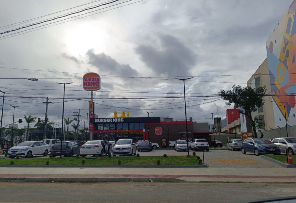 Imagem de uma lanchonete Burguer King com diversos carros estacionados em seu estacionamento. 