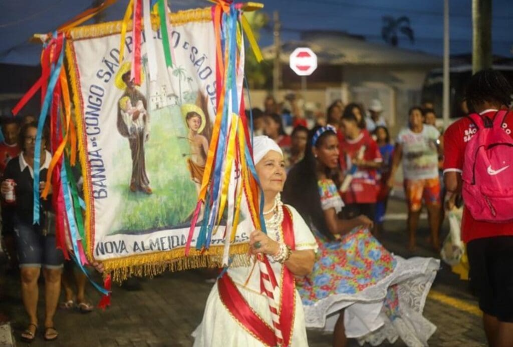 Imagem de uma senhora carregando um estandarte durante as festas de São Benedito e São Sebastião.