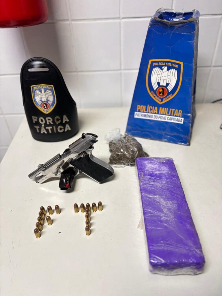 Imagem de uma mesa com uma braçadeira da Força Tática, um material de divulgação da Polícia Militar, uma pistola calibre .380, 17 munições, um tablete de maconha, além de uma porção de maconha.