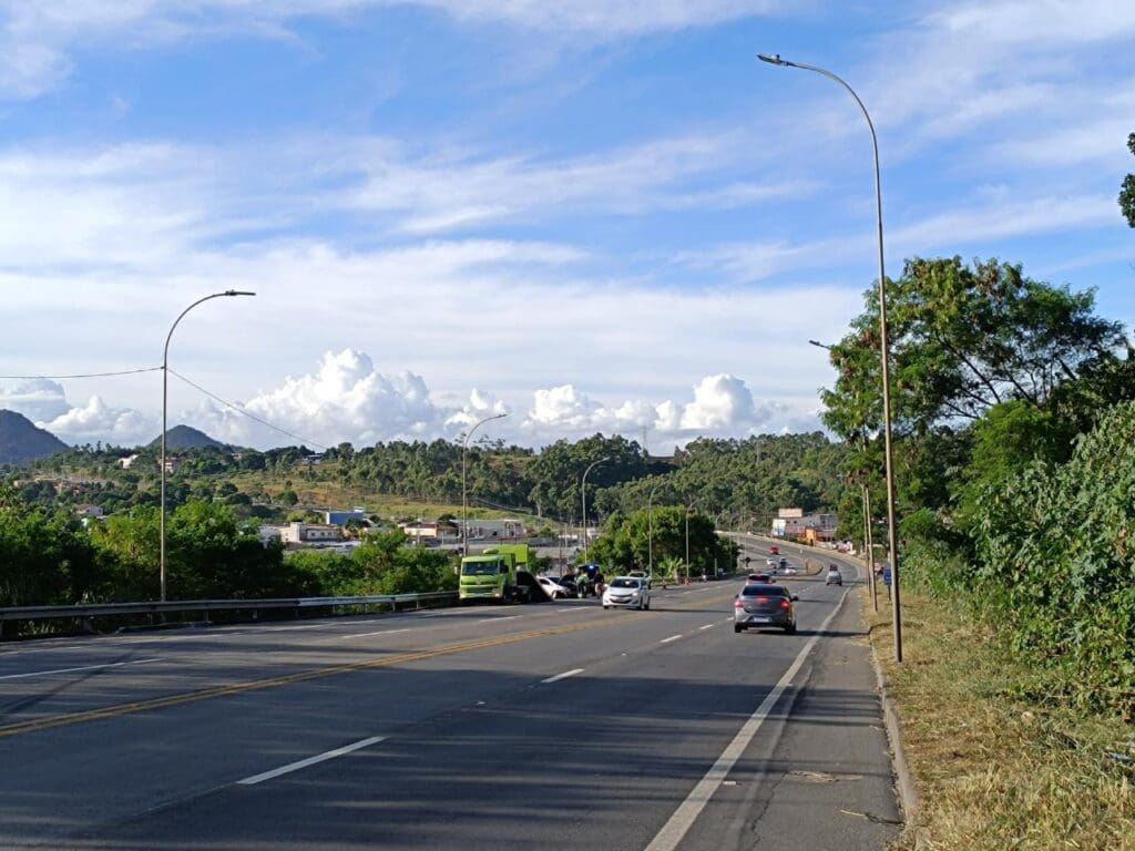 Imagem de uma avenida, com um veículo danificado parado no canteiro, após um acidente, em volta do veiculo agentes da PRF e funcionários de um caminhão guincho, que esta estacionado proximo ao veículo acidentado.