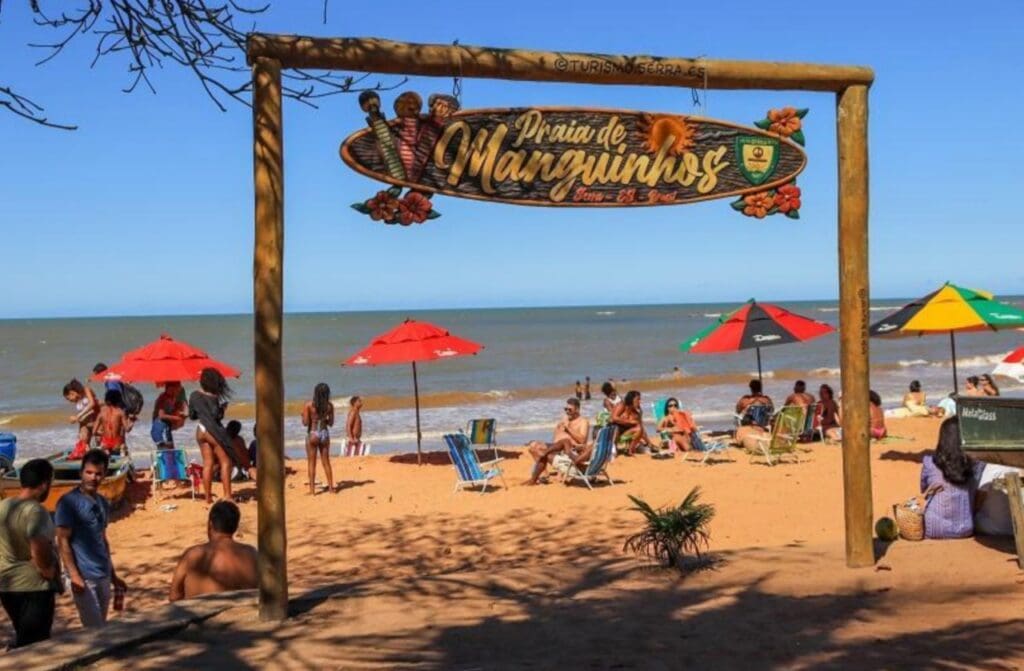Portal da praia de Manguinhos, em destaque e no undo a praia com diversas pessoas na area.