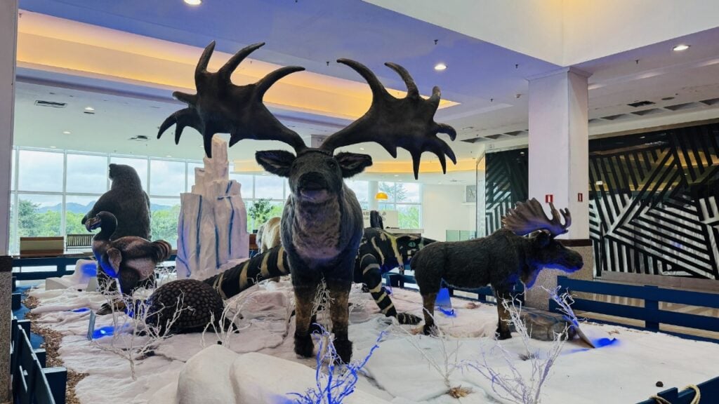 Imagem da Exposição “Gigantes da Era do Gelo”, no saguão de um shopping, com bonecos gigantes de alces e aves Dodô.