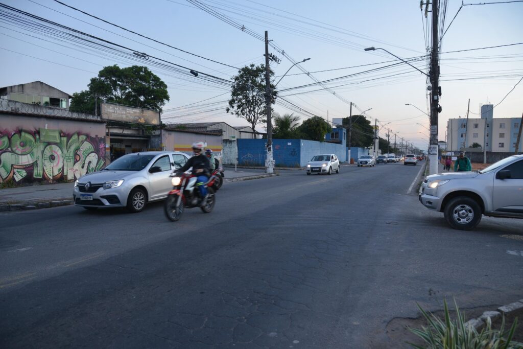 Imagem de uma rua com veículos trafegando pelo local, em destaque um carro ao lado de uma moto.