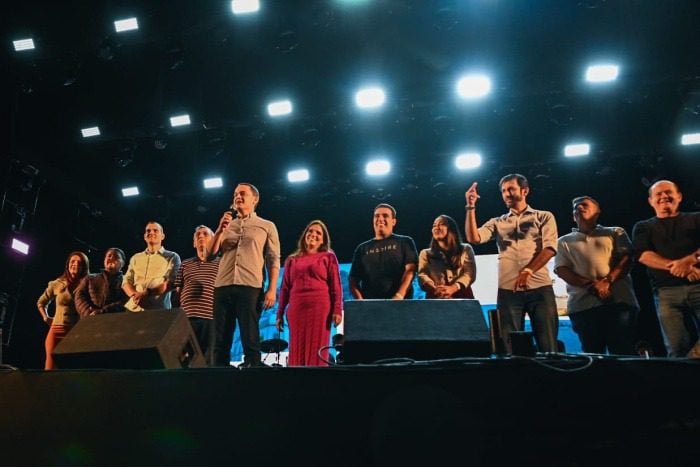 Imagem de um palco com cerca de 11 pessoas durante um discurso do prefeito de Vitória Lorenzo Pazolini.