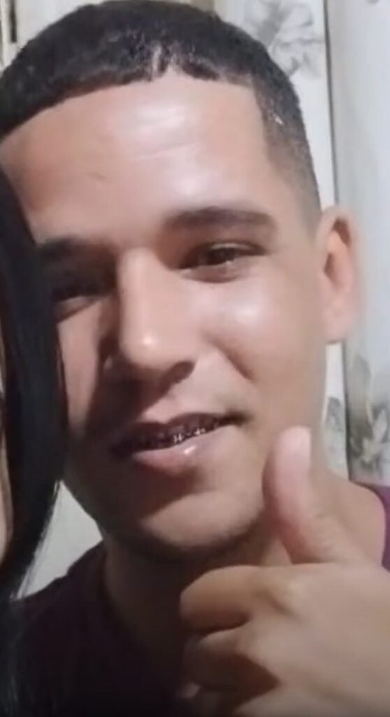 Um homem Denis Mike Leondras Tavares, de 32 anos, fazendo sinal de positivo com uma das mãos.