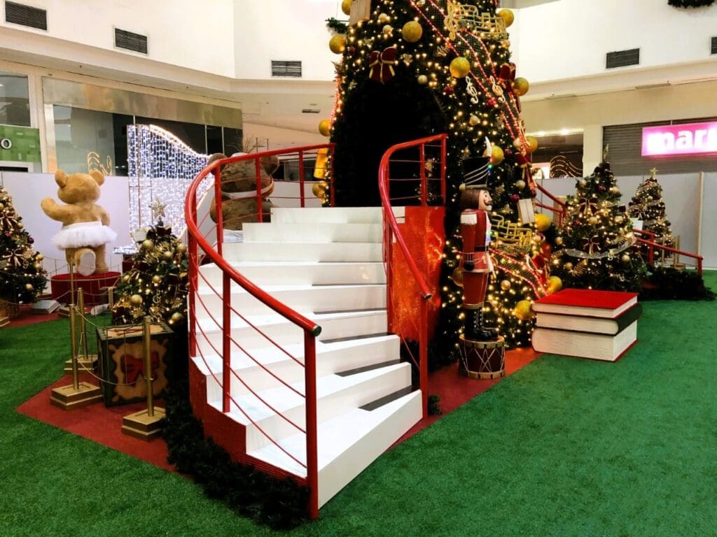 Imagem de um shopping com um local decorado com uma árvore de Natal e uma escada com formato de teclas de piano, além de outros objetos natalinos.