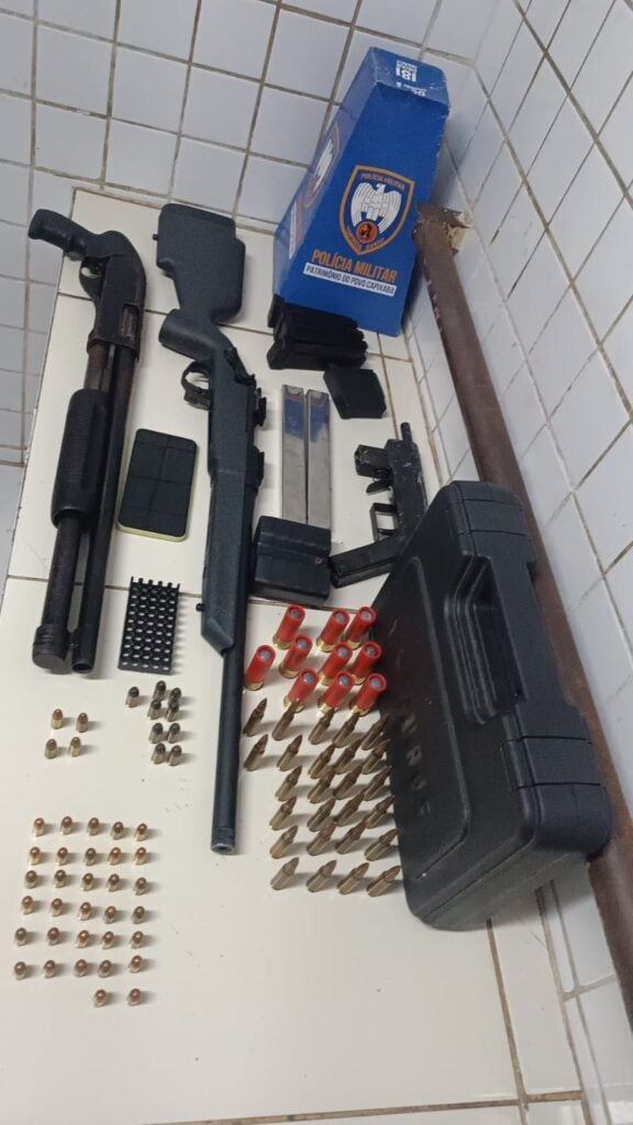 Sobre uma bancada, diversas armas e munições apreendidas pela PM: um fuzil calibre 7,62; uma espingarda calibre 12; uma metralhadora semi-industrial; quatro munições calibre 9mm; dez munições calibre 12; nove munições calibre .40; trinta e duas munições calibre .380; vinte e seis munições calibre 7,62; um carregador para calibre 7,62; três carregadores de pistola PT 845 calibre .45; um carregador CANIK 9mm; um porta-carregador para pistola; uma colmeia para calibre 9mm; dois carregadores de fabricação caseira para calibre 9mm; uma maleta para arma e um aparelho celular apreendido.