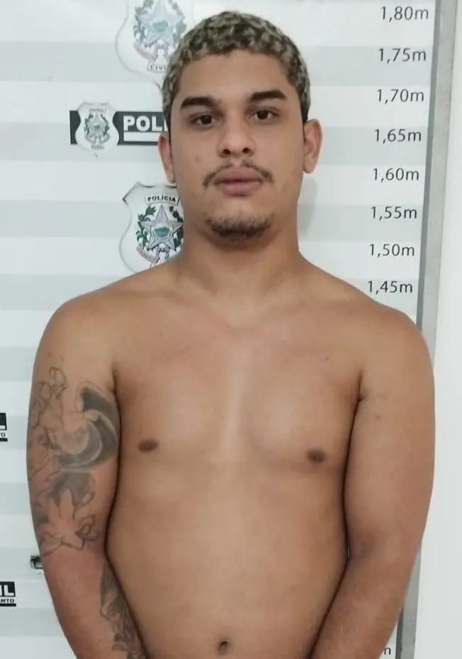 Imagem de um homem (Ryan Gabriel Gomes da Rocha, de 22 anos.), acusado de participar de uma quadrilha de furtos de moto, parado em frente a uma parede onde ha uma marcação de metros, usada pela polícia para realizar a fotografia e identificação de detidos.