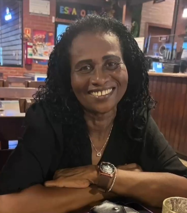 Imagem de uma mulher sorrindo, com os braços sobre uma mesa.