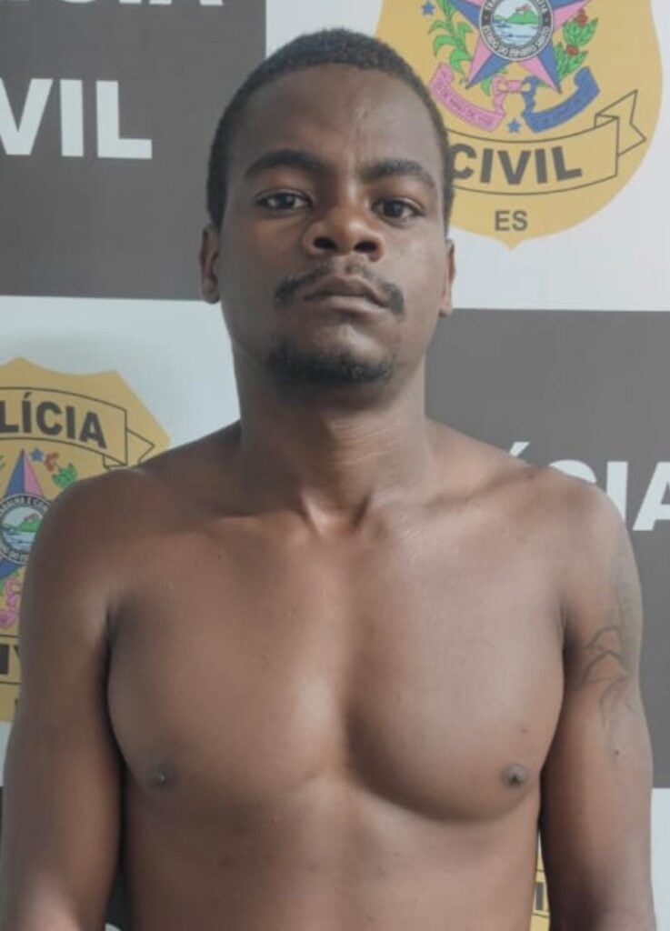 Foto de um sujeito (André Makalle Falcão dos Santos, de 27 anos) em frente a uma parede com identificações da Polícia Civil.